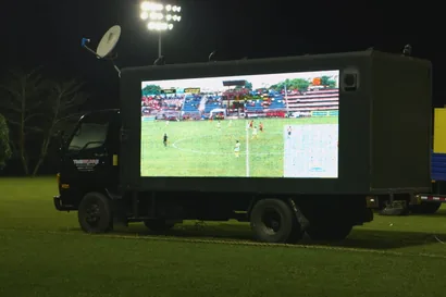 Timesquare LED truck parked on a floodlit sports field, its screen showing a live football match